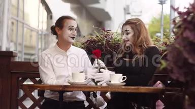两个快乐的哑剧在咖啡馆里约会。 快乐的男人给他的女朋友送花。 浪漫的约会